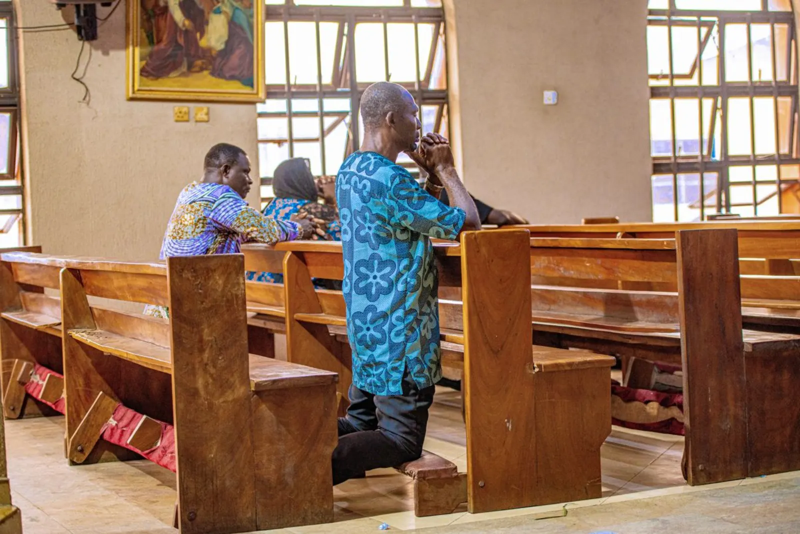 Members of a congregation kneeling in prayer between wooden pews